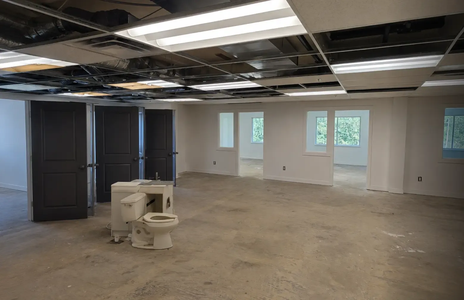 Before picture of a commercial open office workspace undergoing major interior renovation by Pacific Coast Contracting, showing exposed ceiling grids, unfinished concrete floors, and demolition materials.